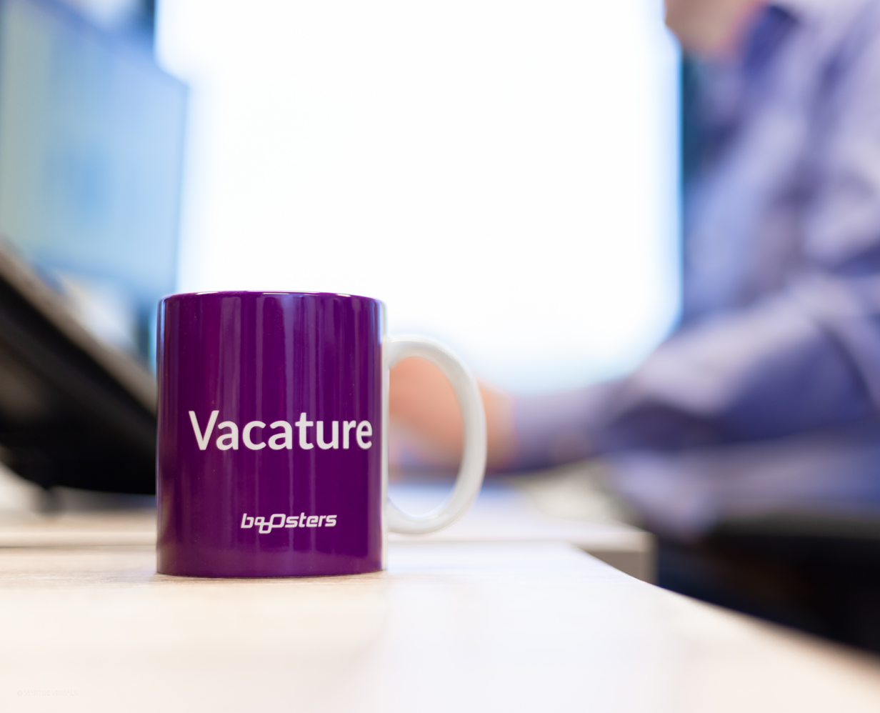 Booosters koffiemok met daarop de tekst 'Vacature' op een bureau op het Booosterskantoor
