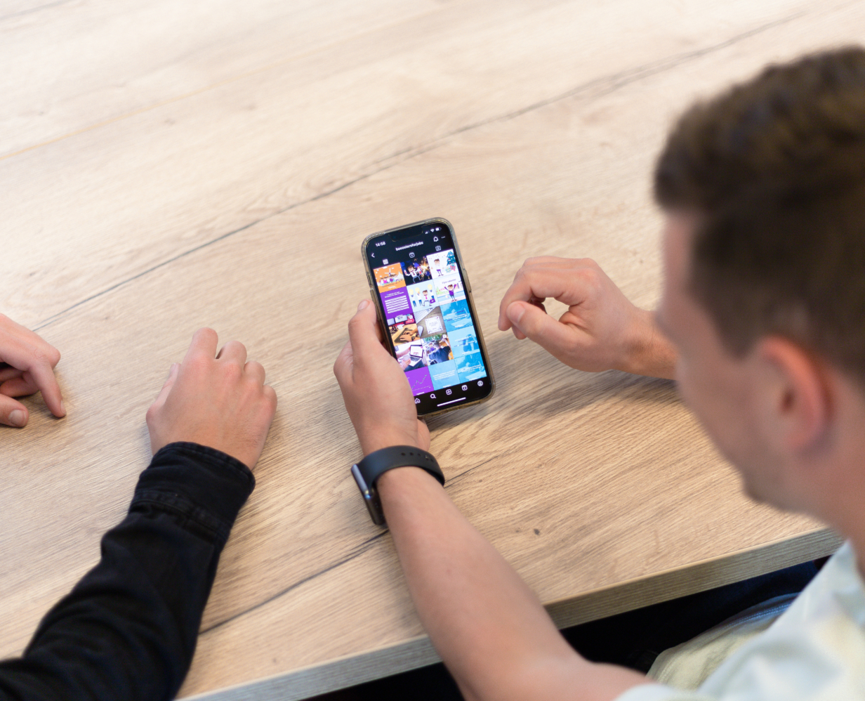 2 Booosters collega's kijken samen naar een telefoon met daarop een social media kanaal